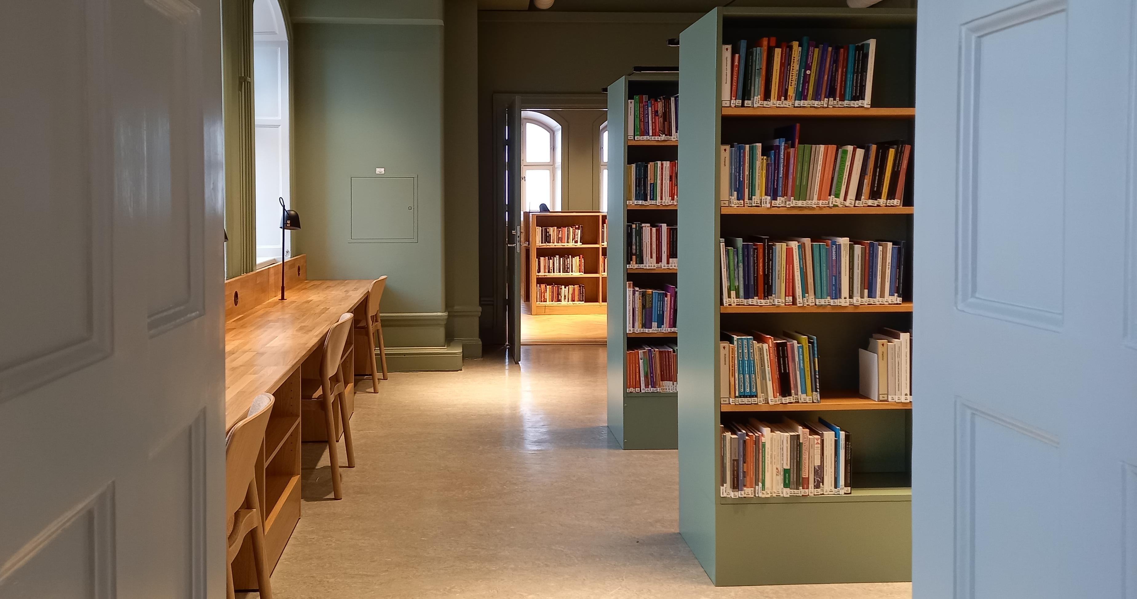 Bibliotekets milt gröna tysta lässal med träfärgade bord, stolar och bokhyllor